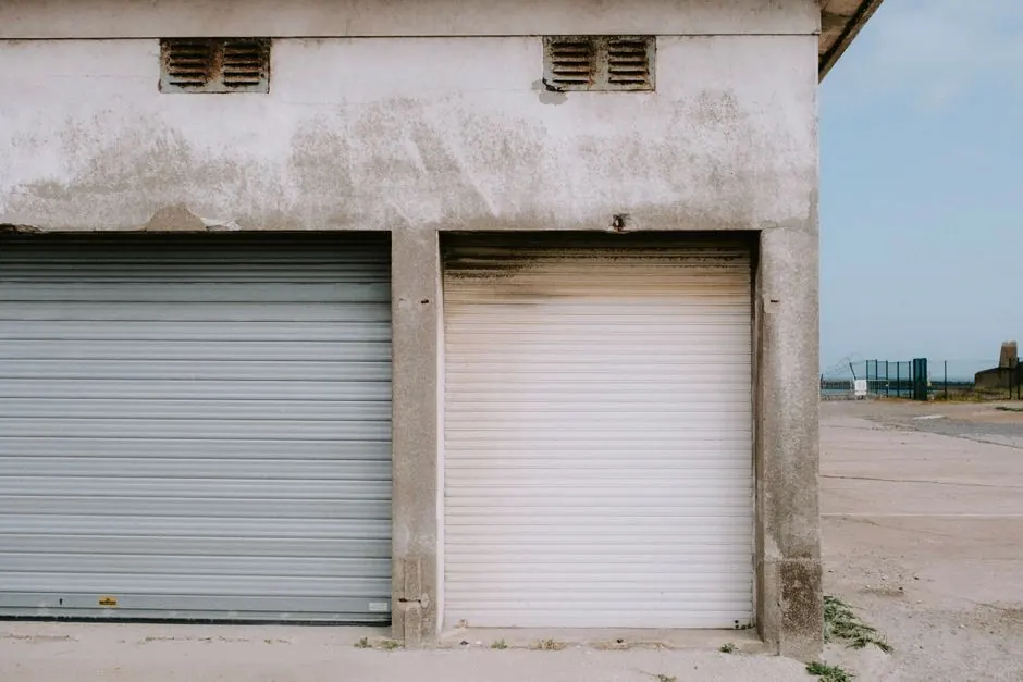A detailed view of a weathered industrial building façade with rusty roll-up doors and a concrete exterior.